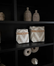 Grote luxe offermanden in een vakkenkast. De offermanden zijn handgemaakt in Indonesië. De offermanden hebben kralen in crème en beige kleuren, en er zitten kauri schelpen op. 